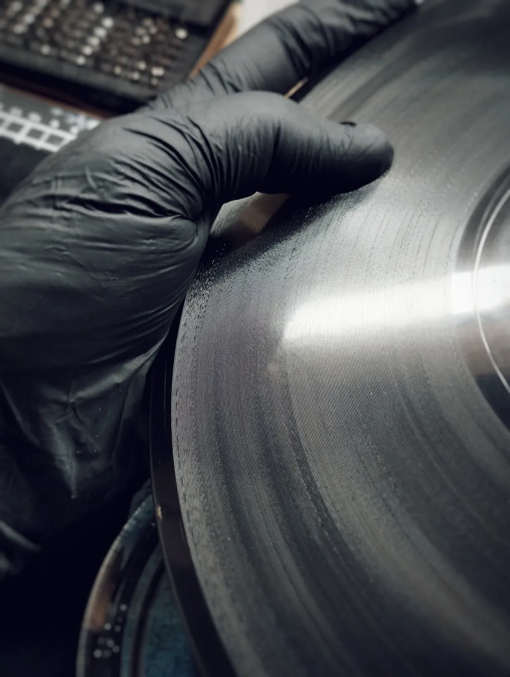 Mão com luva a segurar um disco, com os sulcos a refletir a luz